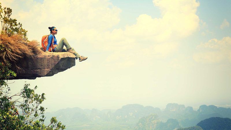 smiling woman rests on cliff edge after hike|You'll-Age-Better-if-You-Have-This-One-Simple-Thing,-According-to-Science_554390080_Monkey-Business-Images