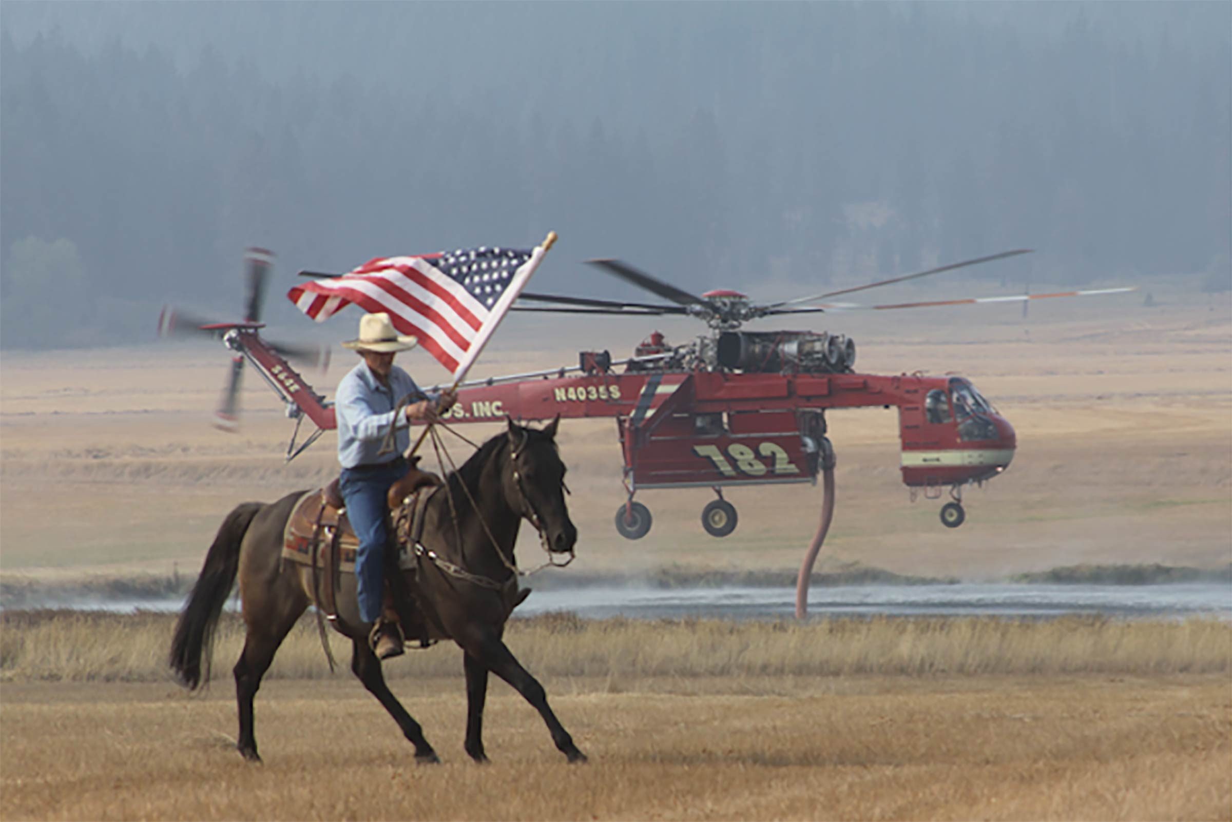 a man on a horse waves an american flag to show support for the fire department helicopter in the background