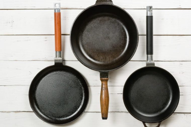 Several empty cast-iron frying pans on a white wooden background. View from above. Space for text.