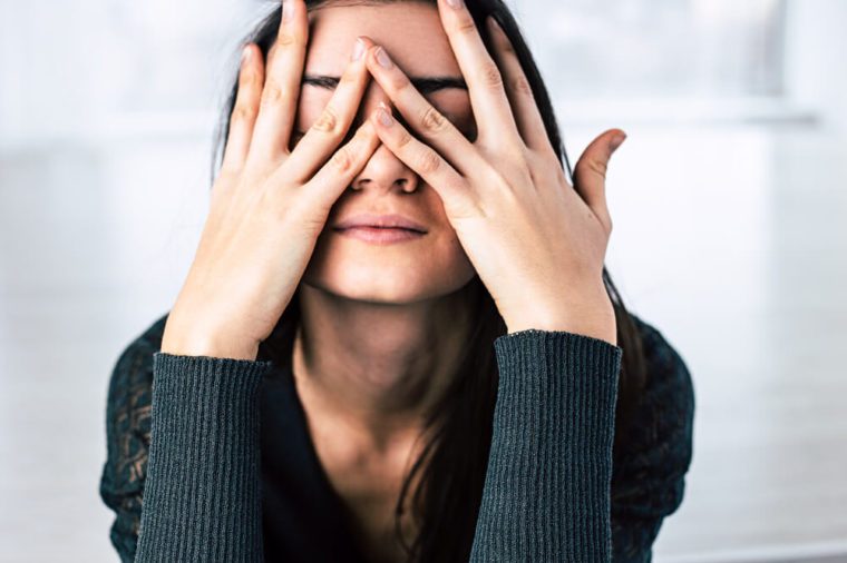 Dark-haired girl covers her face with hands