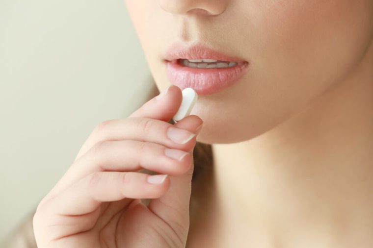 Beautiful young woman taking pill, closeup