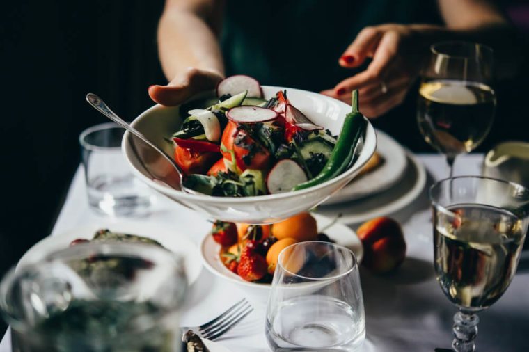 Hands passing over a bowl of salad served during a dinner of a party in a restaurant.