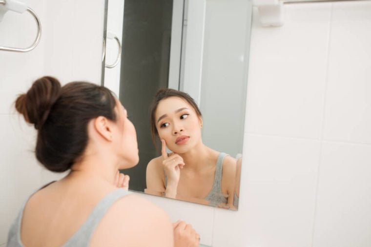 거울을 들고 얼굴을 만지고 걱정하는 아시아 여성