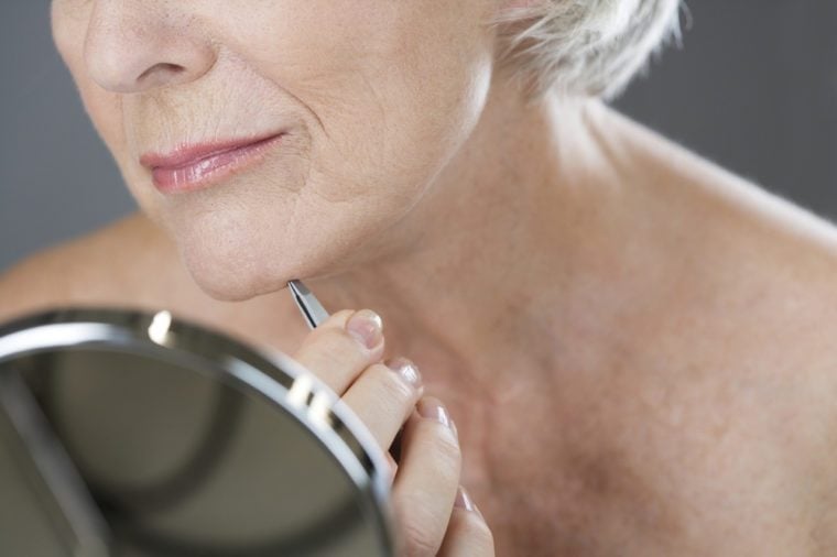 A senior woman plucking hairs from her chin with tweezers