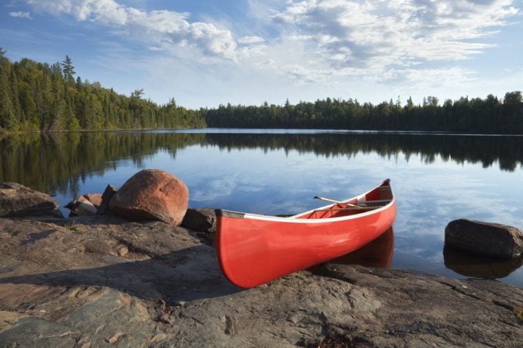 A red canoe rests on a rocky shore of a calm blue lake in the Boundary Waters of Minnesota