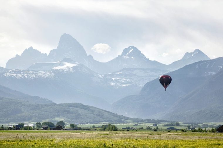 A view of a hot air balloon floating over the Idaho country side, in front of the Grand Teton on a hazy morning.