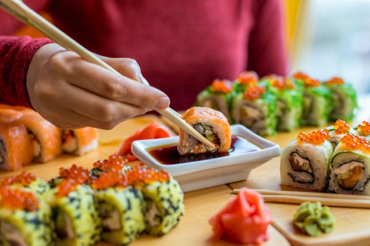 Woman eating sushi rolls at the table - close up photo. Traditional Japanese oriental kitchen with raw fish.