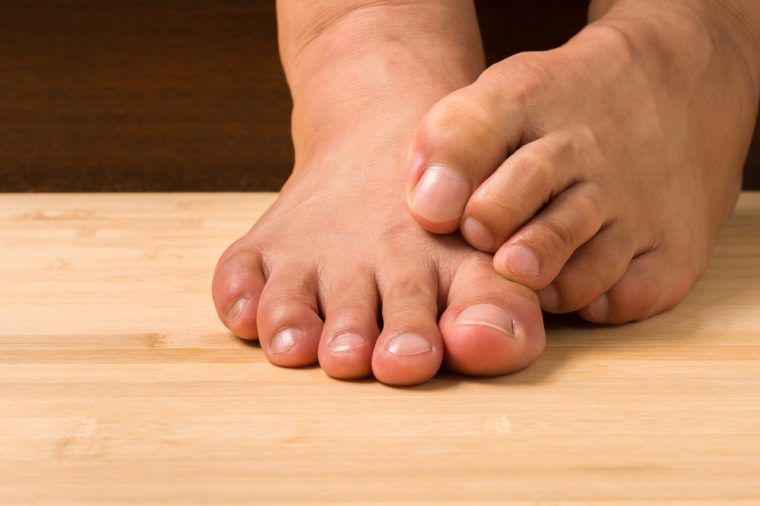 Closeup a man with itchy feet uses his big toe to scratch his other foot on wooden floor.