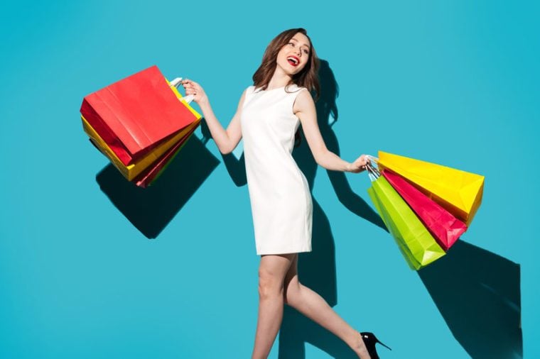 Full length portrait of a beautiful smiling woman in dress walking with colorful shopping bags isolated over blue background