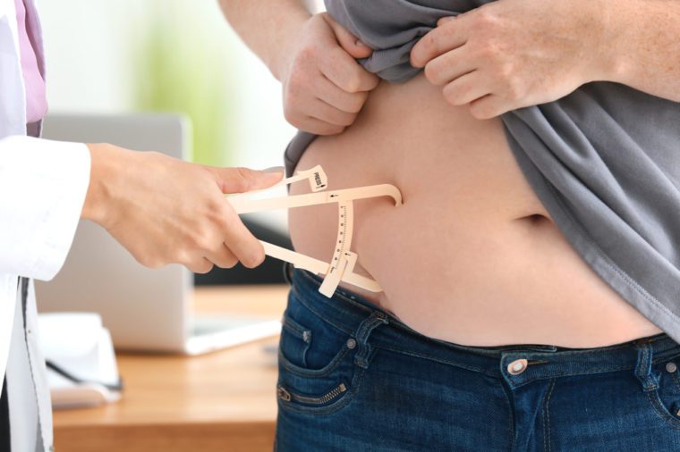 Young female doctor measuring fat layer of overweight woman with caliper in clinic