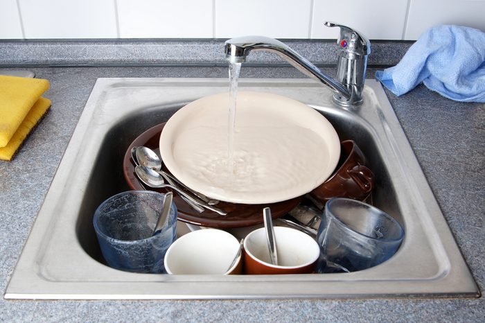 pile of dirty dishes in kitchen sink with running water
