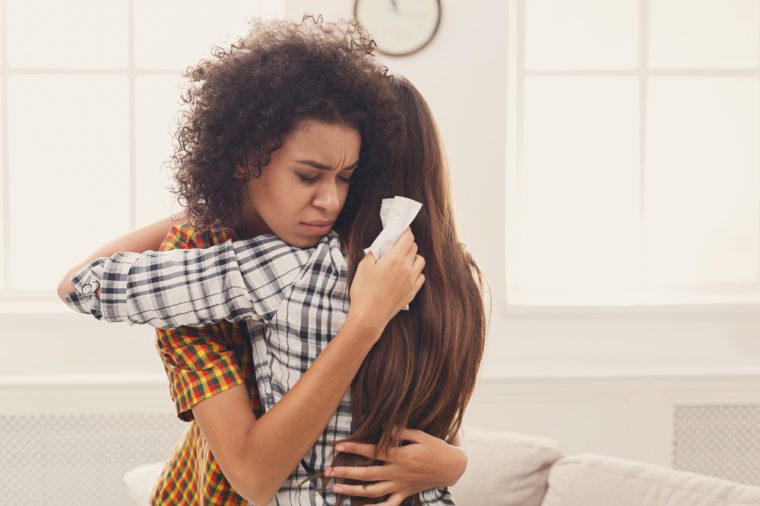 Woman hugging her depressed friend at home, closeup. Young girl supporting her crying girlfriend. Friendship consoling and care, copy space