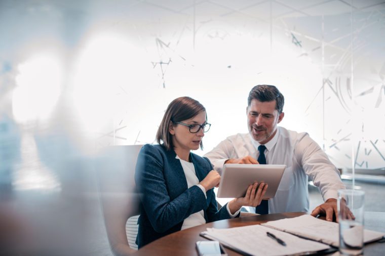 Two confident businesspeople using a digital tablet together while working at a table in a modern office