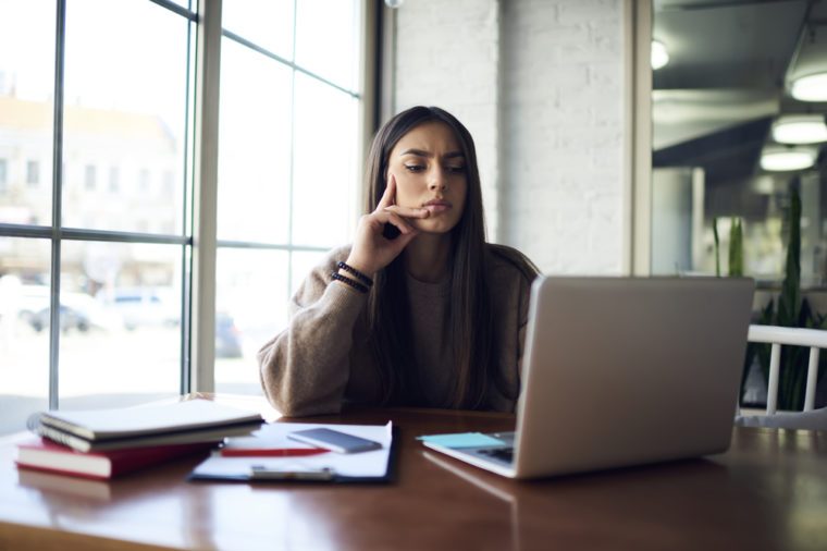 Thoughtful brunette student watching training webinar while preparing for examination learning new information, talented writer pondering on new movie on laptop computer creating article review