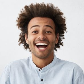 Carefree joyful handsome Afro American man with bushy hairstyle and bristle having shining eyes opening his mouth with joy bursting into laughing. Positive human expressions, emotions and feelings