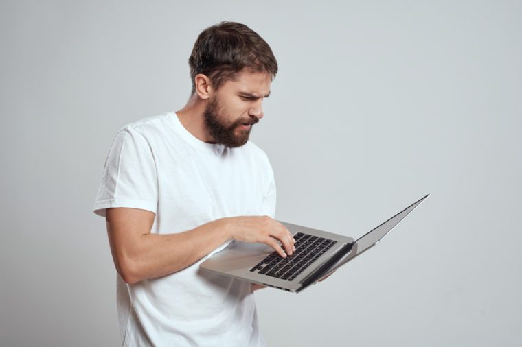  serious man with a beard working behind a laptop on a gray background 