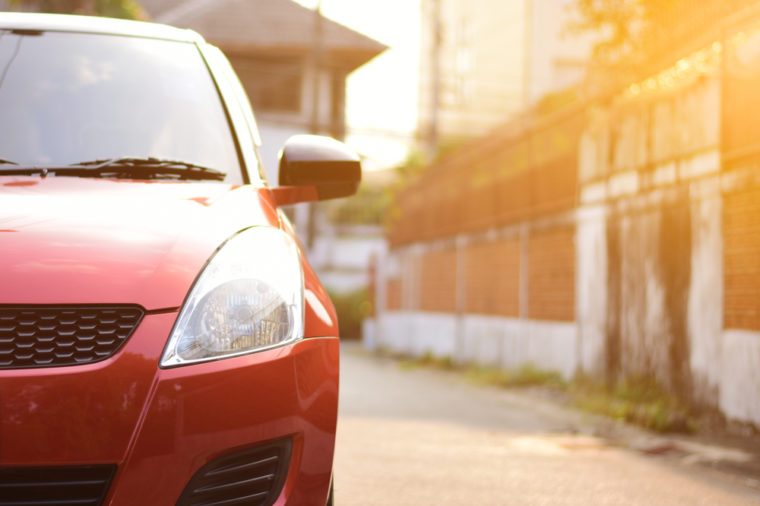 Focusing on the red car headlights on a street corner with sunlight flares. In the background, village and street. Closeup headlights of car.