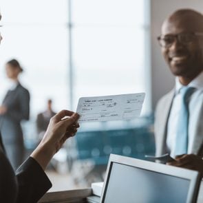 close-up shot of smiling african american businessman giving passport to staff at airport check in counter