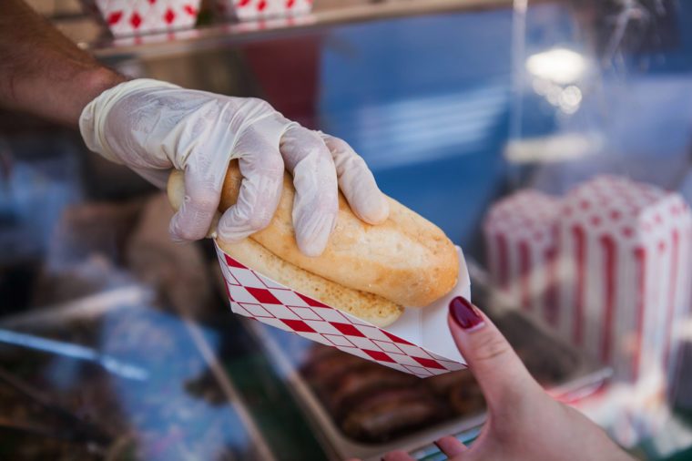 Street stall to sell hot dogs. Customer holding a hot dog purchased. 