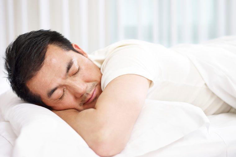   An Asian man lying on the bed in his bed. 