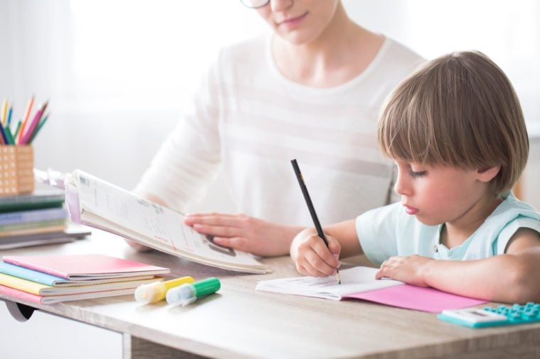 Smart child doing homework at a desk with support of a tutor