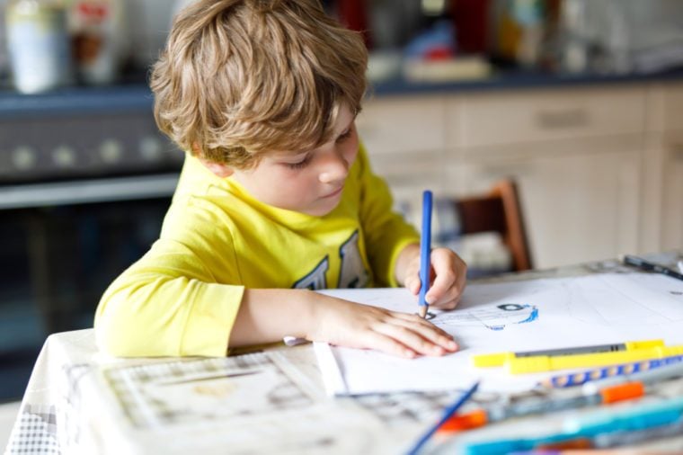 Tired kid boy at home making homework writing letters with colorful pens