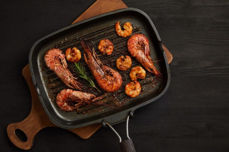 top view of grilled shrimps with rosemary on wooden cutting board on black tabletop