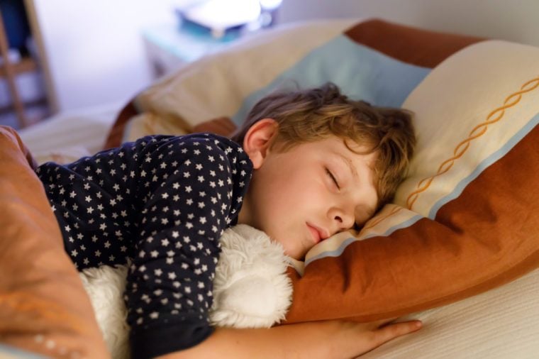 Little preschool kid boy sleeping in bed with colorful lamp.