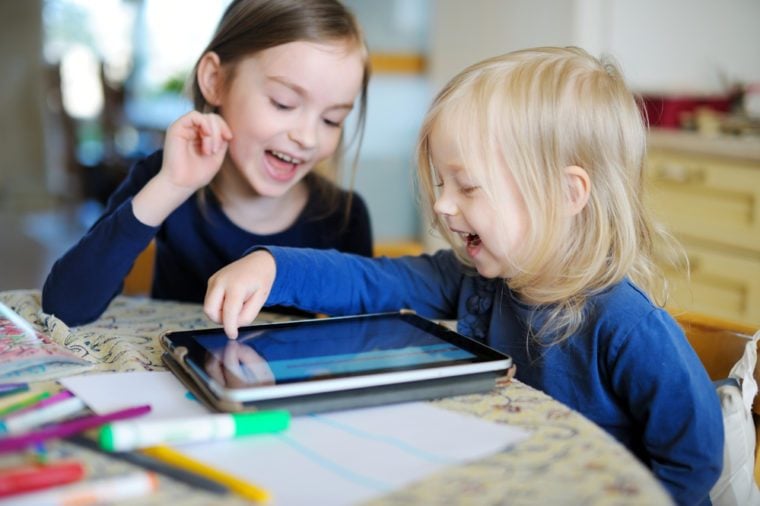 Two adorable little sisters playing with a digital tablet at home