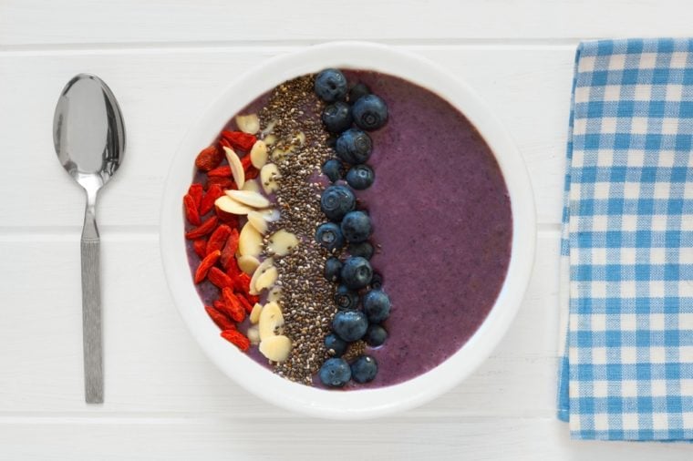 Nutritious blueberry smoothie bowl with goji berries, almonds and chia seeds on white wood with cloth and spoon