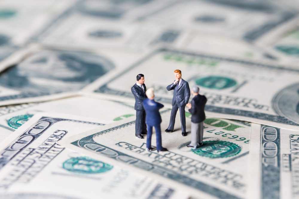 Miniature figurine toys standing on dollar with money and work concept. Focus on the businessman.