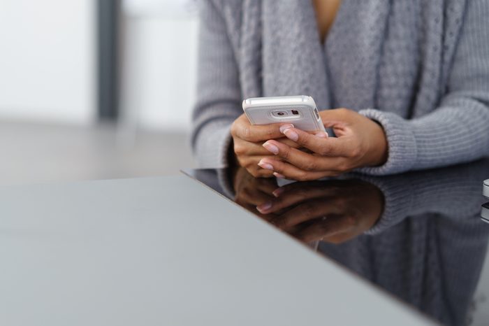 Young African American woman using a mobile phone to send or receive text, close up of her hands seated at a table