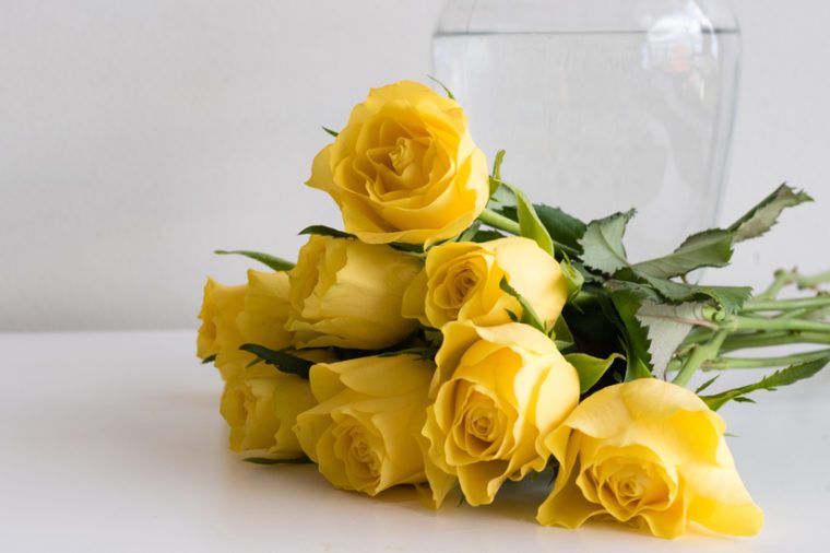 Yellow roses on white table next to glass vase (selective focus)