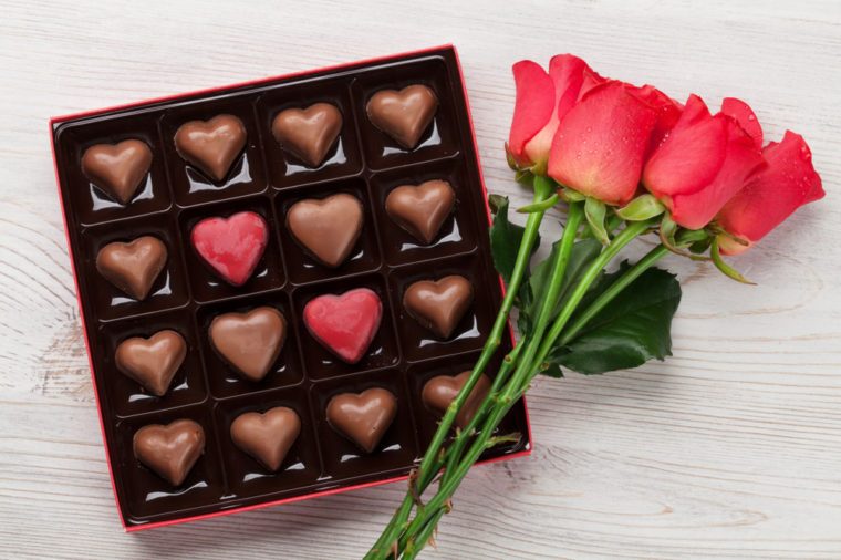 Valentines day greeting card with red roses and heart shaped chocolate on wooden background. Top view