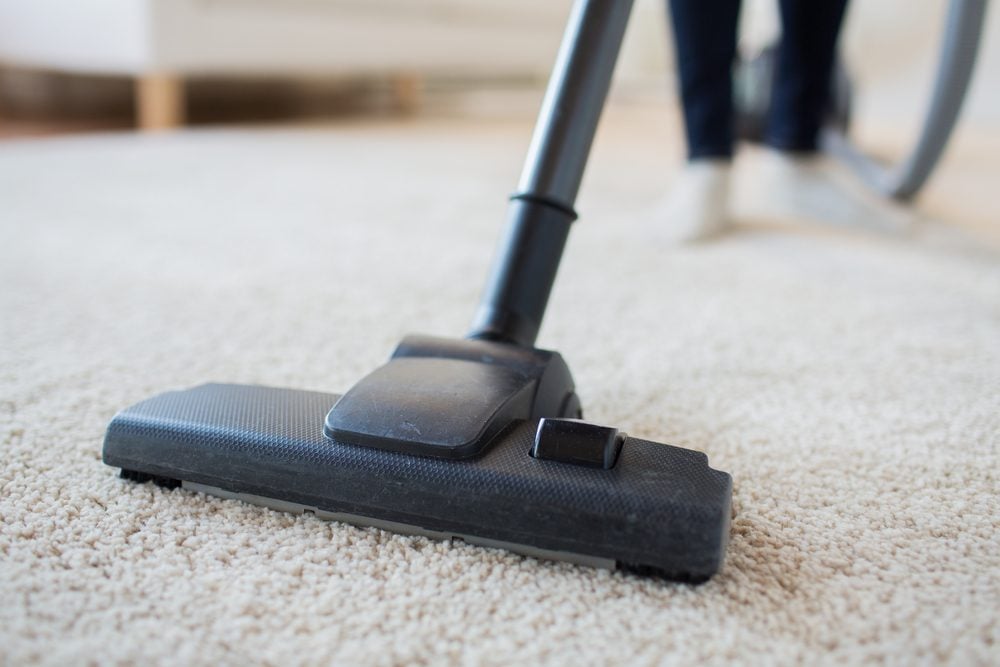 people, housework and housekeeping concept - close up of woman with legs vacuum cleaner cleaning carpet at home