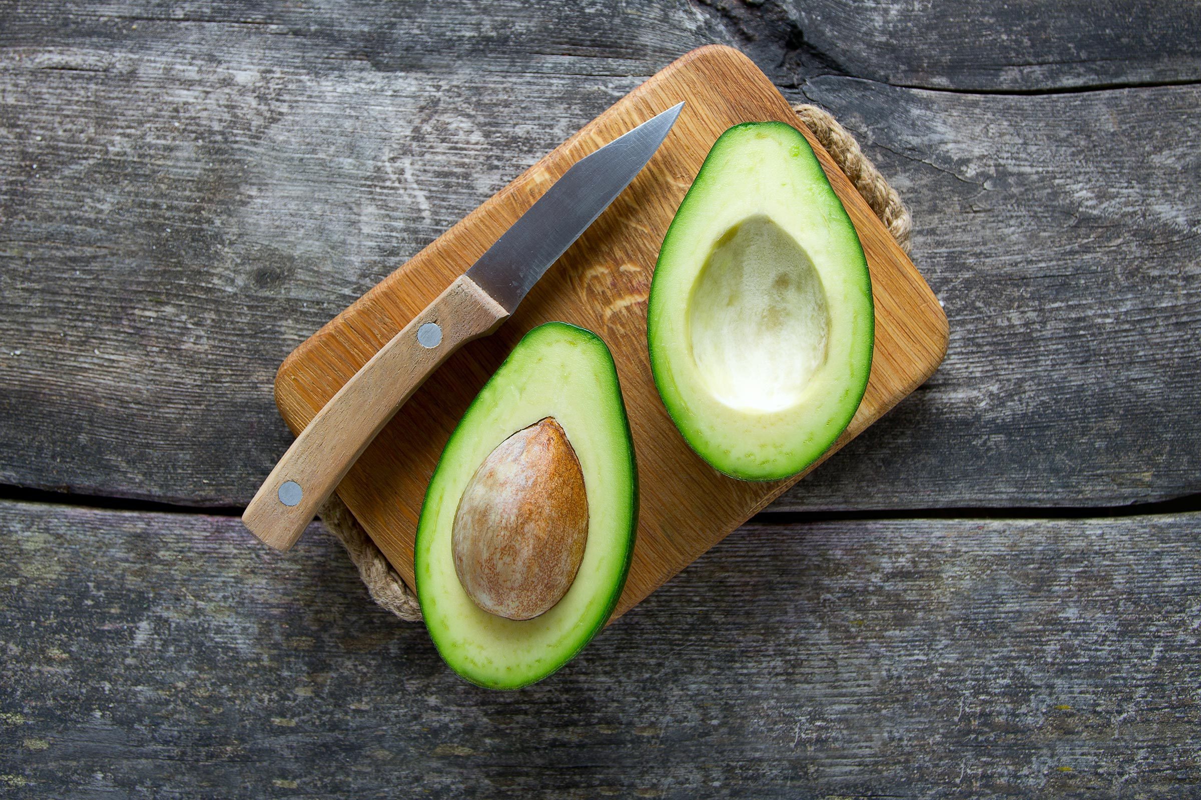 Fresh Market Avocado Cut In Half On A Wooden Cutting Board Next To A Knife  With More Avocados In The Background In A Cotton Reusable Shopping Bag  Stock Photo - Download Image