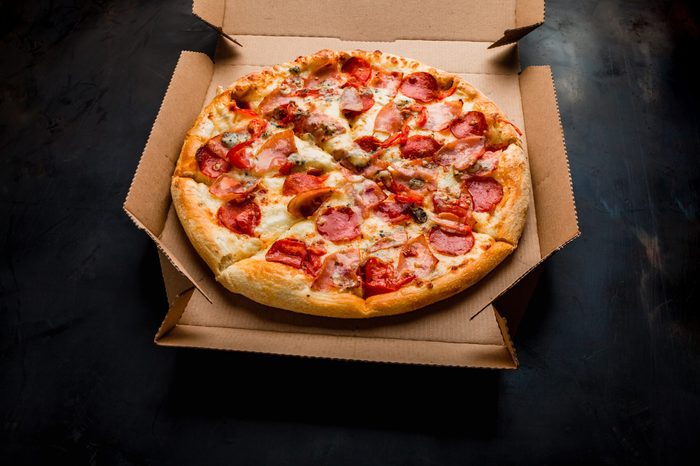 Pizza in a cardboard box against a dark background. Close-up. View from above. Pizza delivery. Pizza menu.