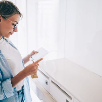 Positive caucasian young woman holding received envelope checking mail from metal letterbox in apartment,pretty caucasian hipster girl in spectacles reading correspondence from postal delivery