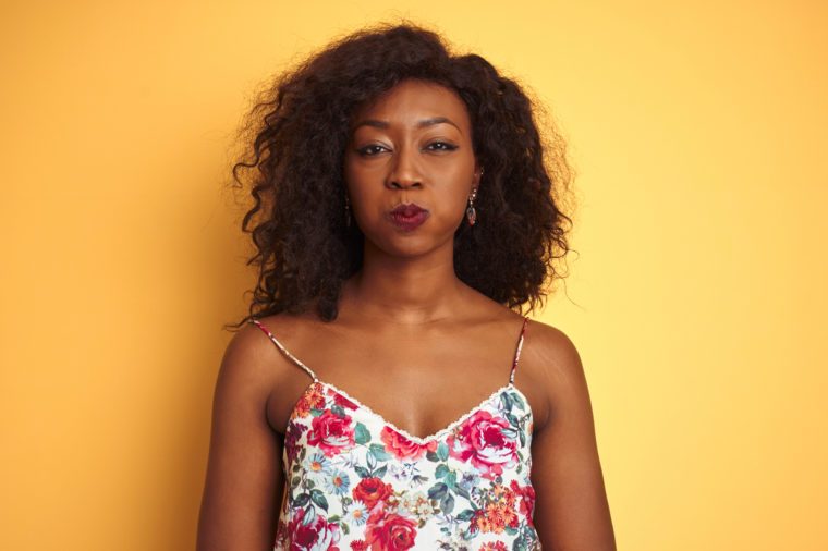 African american woman wearing floral summer t-shirt over isolated yellow background puffing cheeks with funny face. Mouth inflated with air, crazy expression.