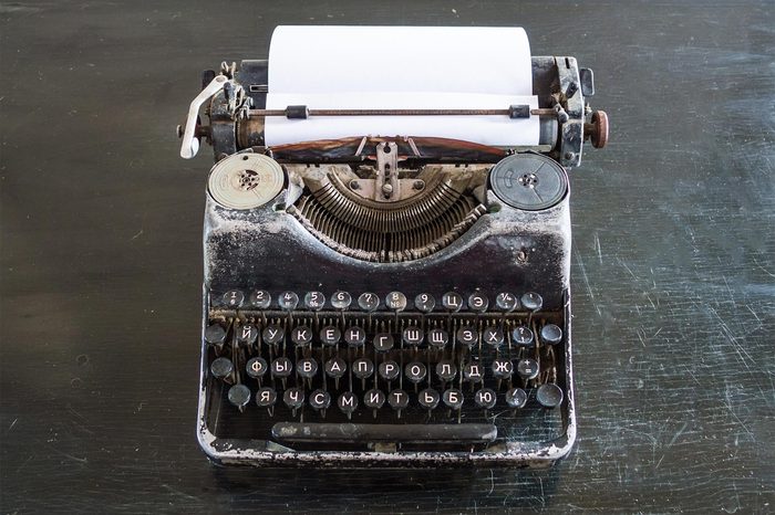 An old typewriter on an old black table with a sheet of paper.