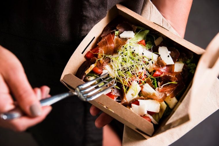 Woman's hand is holding a take away fresh salad in a lunch box. Gourmet conception.