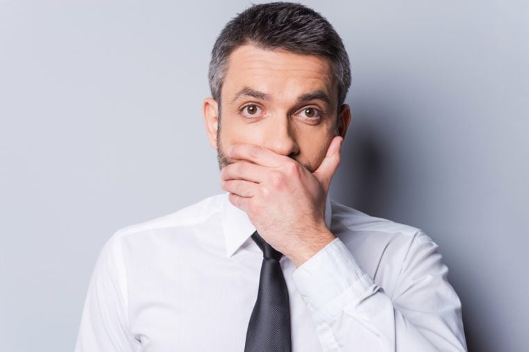 man in a shirt and tie covering his mouth with one hand. gray background.