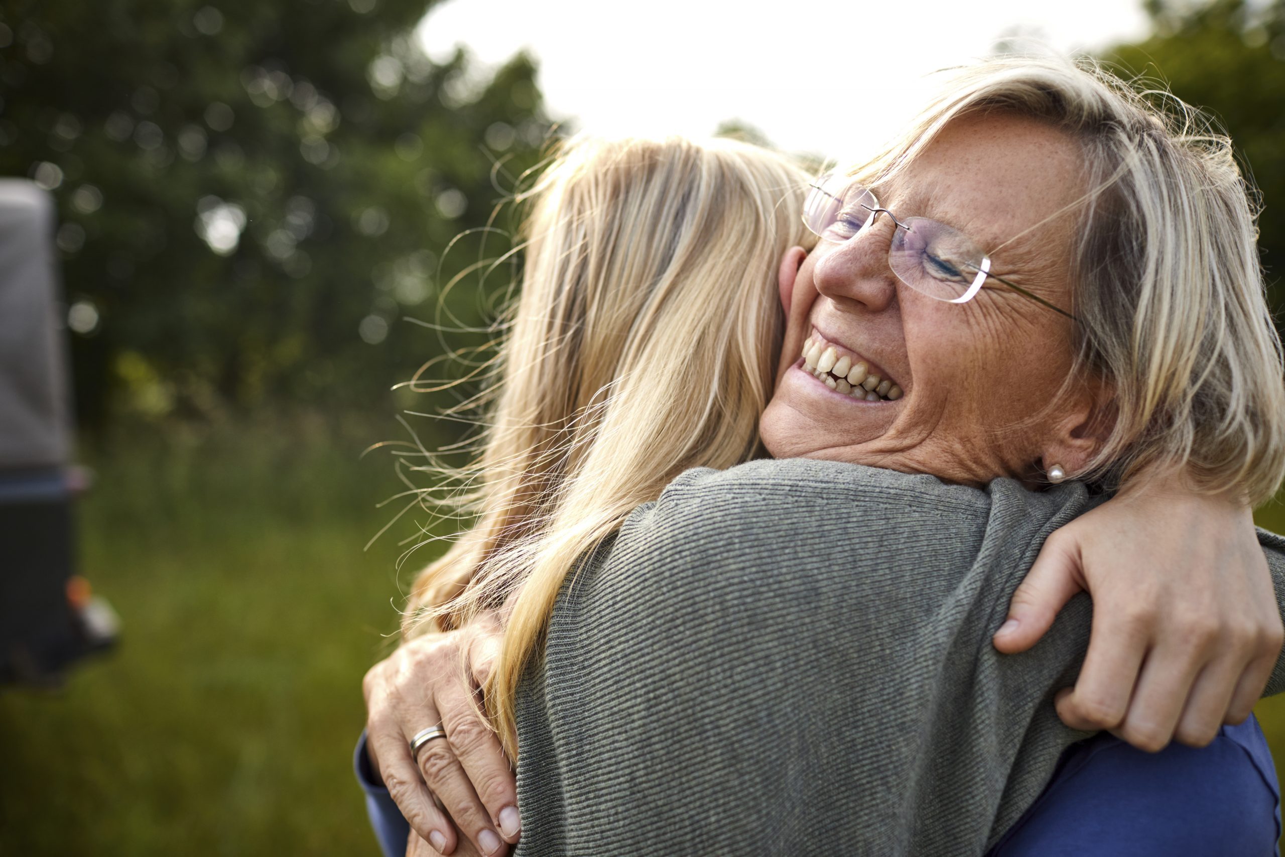 Happy senior woman and young woman hugging outdoors with a jeep in background