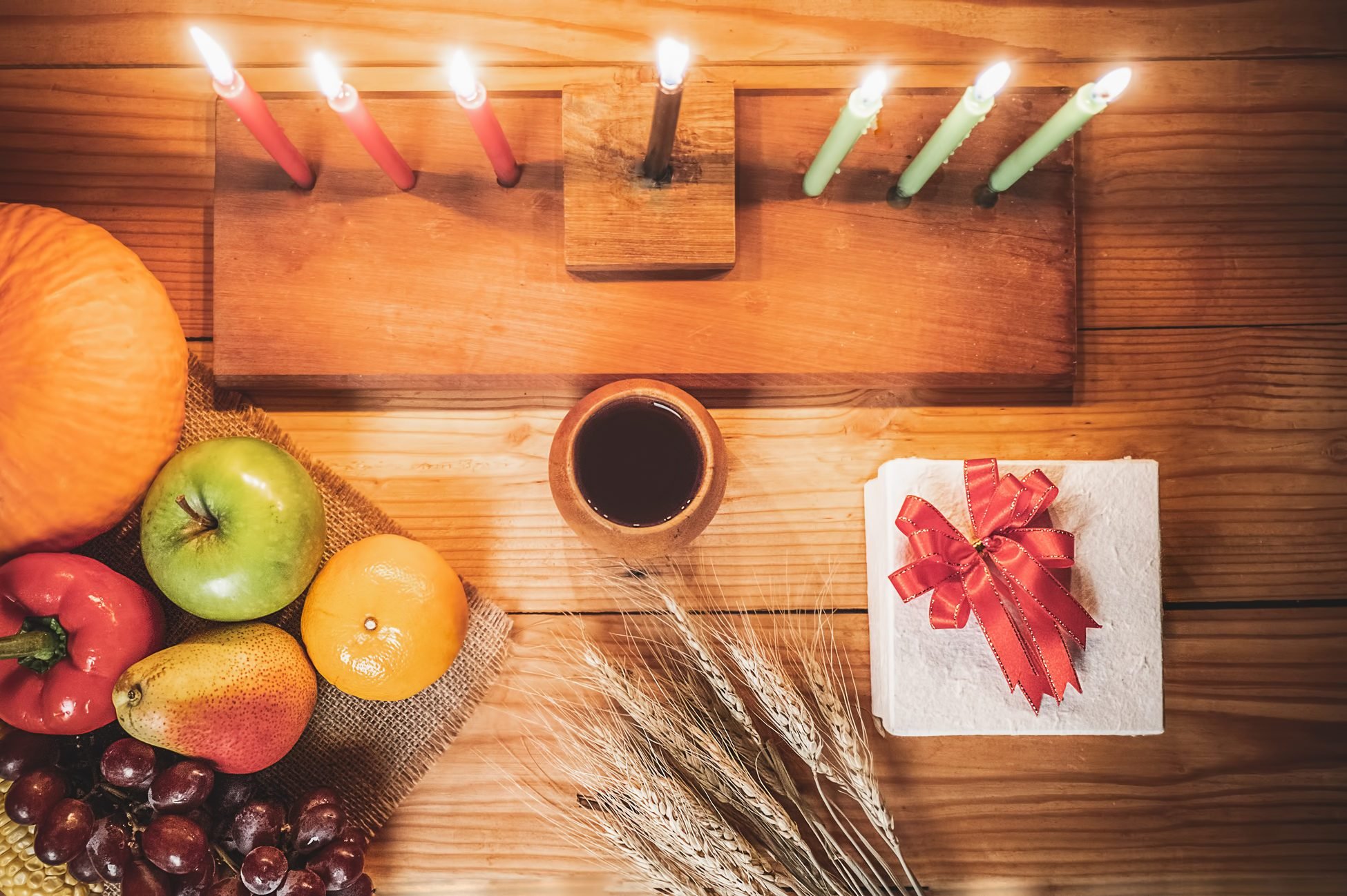 Kwanzaa holiday concept with decorate seven candles red, black and green, gift box, pumpkin,corn and fruit on wooden desk and background.