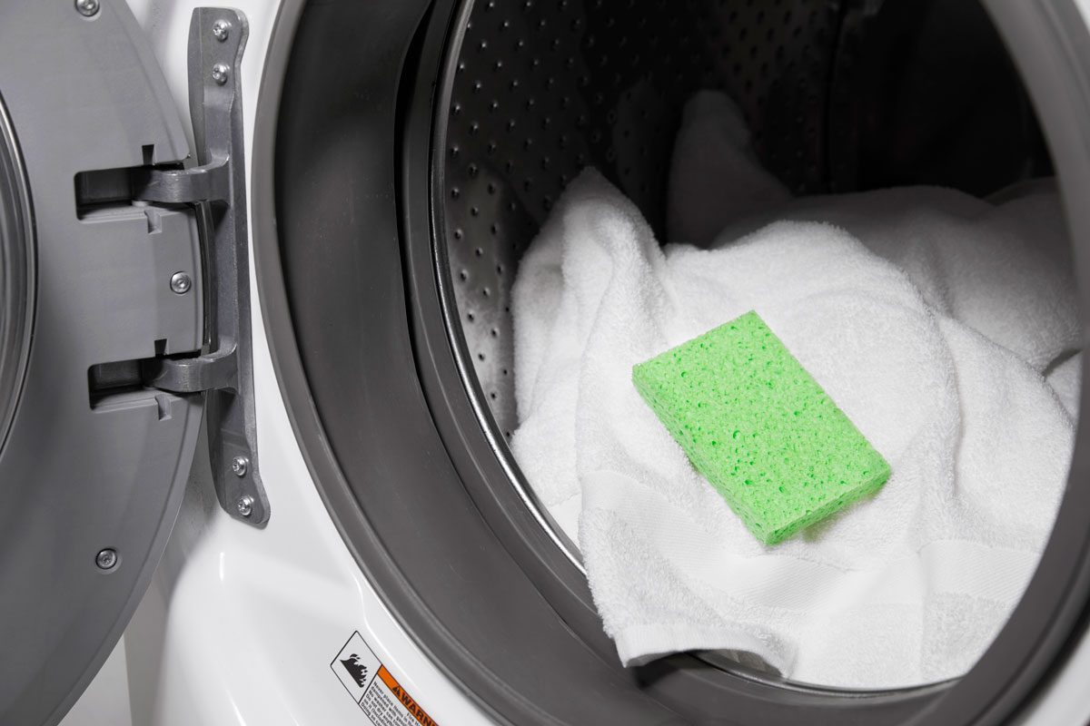 A green sponge is seen in an open washing machine on top of a few white towels