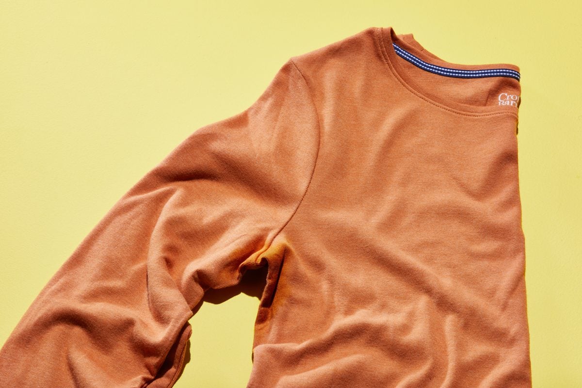 orange long sleeve shirt with underarm sweat stain on a yellow background