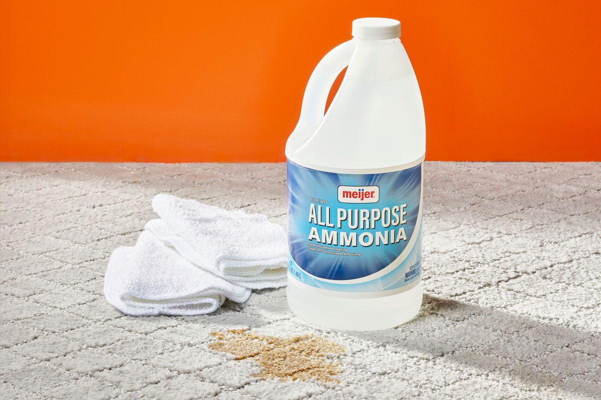 Ammonia bottle and two white cleaning cloths next to a stain on a light gray carpet for Homemade Ammonia Carpet Cleaner
