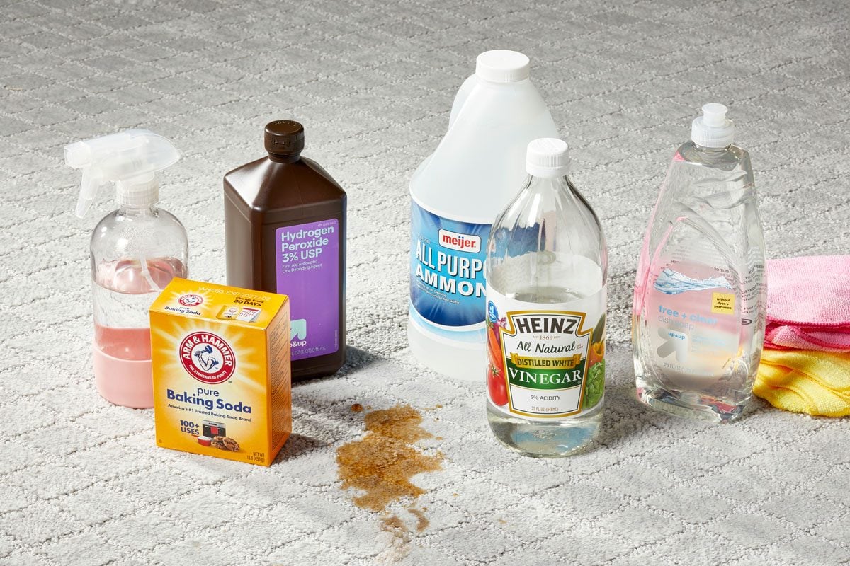 various ingredients for homemade carpet cleaners arranged around a stain on a light gray carpet