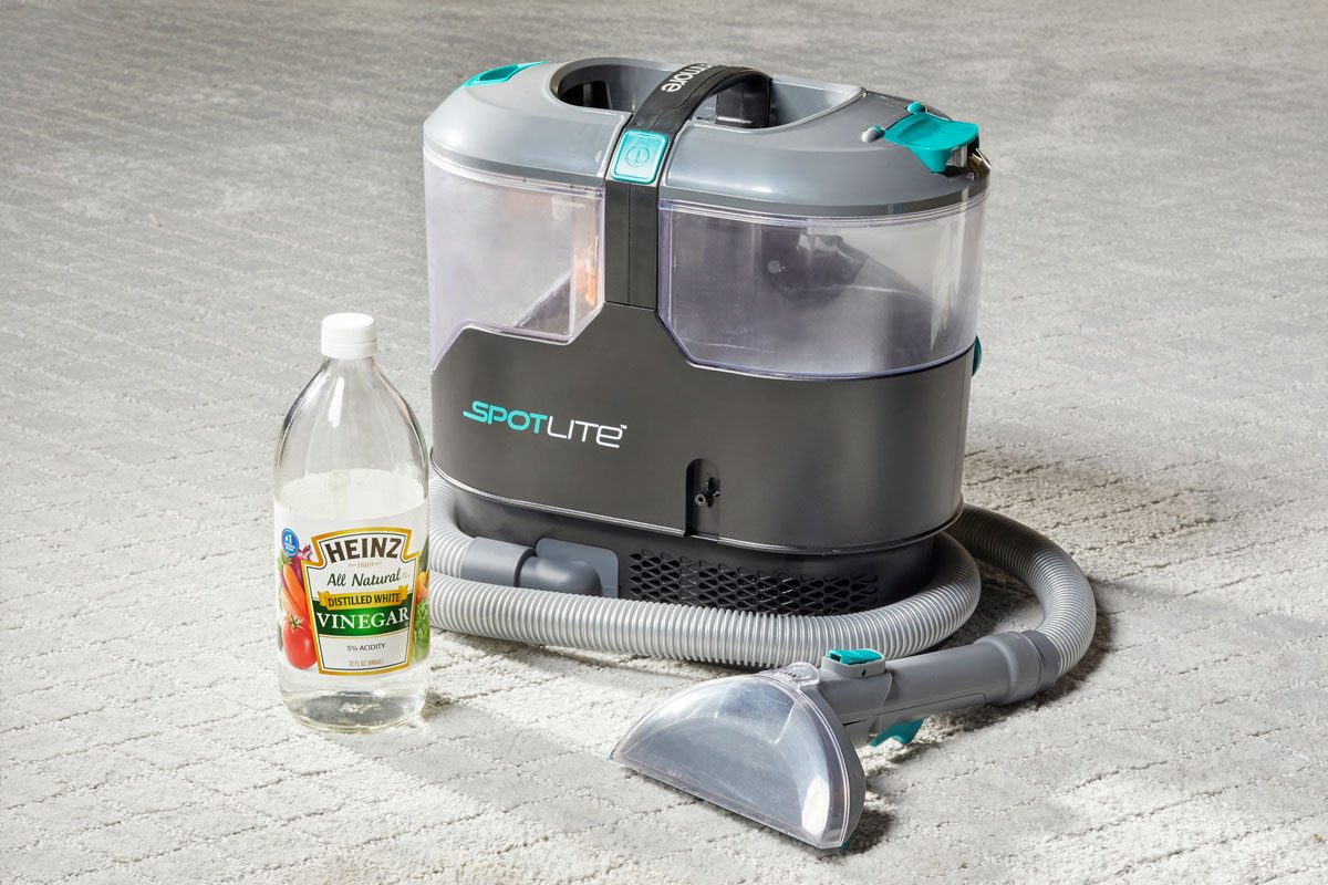 bottle of vinegar next to a carpet cleaning machine on a light gray carpet