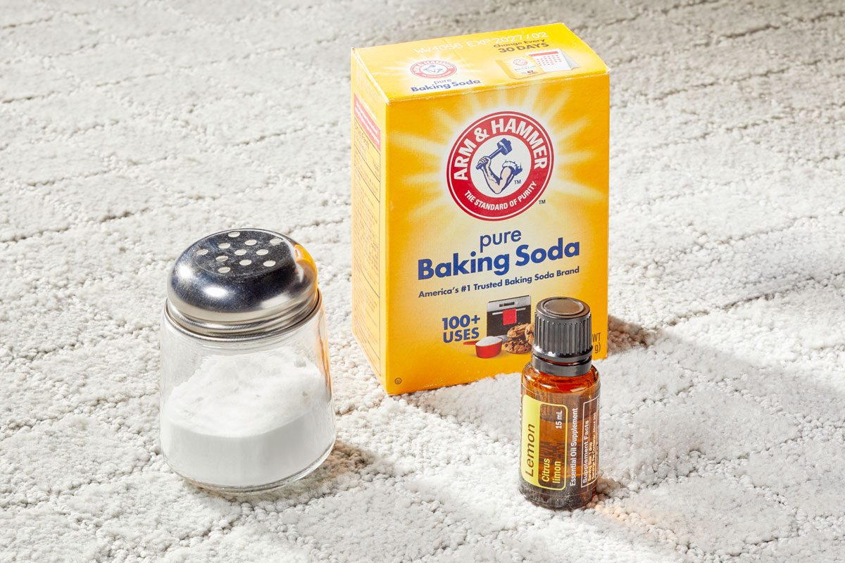 Homemade Carpet Deodorizer in a shaker next to baking soda box and essential oils vial on light gray carpet